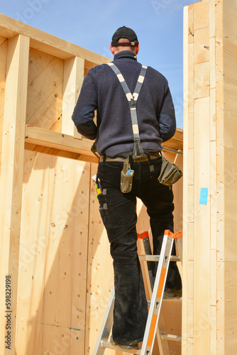 Zimmermann in typischer Arbeitskleidung beim Aufstellen eines Vollholz-Elementhauses photo