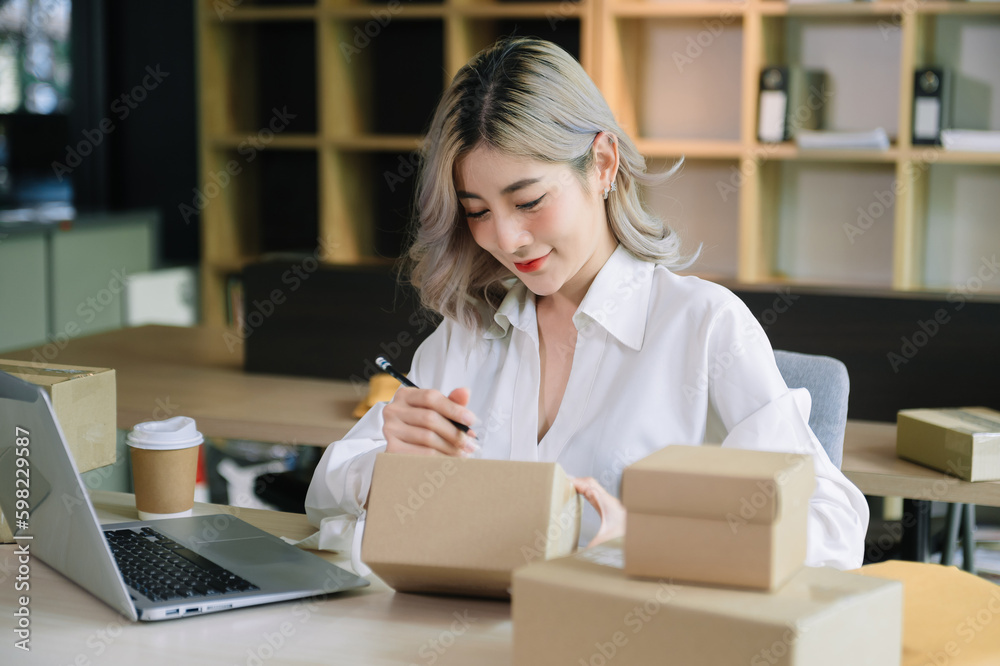 Startup small business SME, Entrepreneur owner woman using smartphone or tablet taking receive and checking online purchase shopping order to preparing pack product box. . Startup small business SME, Entrepreneur owner woman using smartphone or tablet taking receive and checking online purchase shopping order to preparing pack product box. .