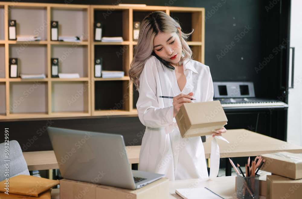 Startup small business SME, Entrepreneur owner woman using smartphone or tablet taking receive and checking online purchase shopping order to preparing pack product box. .
