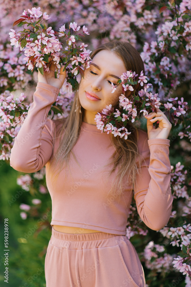 Obraz premium A beautiful young woman enjoys life in a spring blooming garden against the background of blooming apple trees.