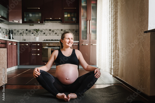 Portrait of young pregnant female exercising out at home. Prenatal groins stretch. Buddha Konasana Pose. Pregnancy yoga and fitness. Happy calm woman deep breath with fresh air lotus pose comfortably.