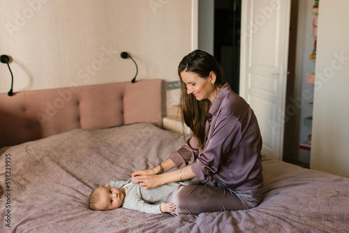 Mother dressing her newborn baby son lying on bed