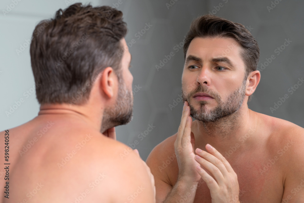 Close-up portrait of perfect brunet man touching chin and skin. Handsome man touching face in front of the mirror in bath. Perfect skin. Man cosmetic, skin treatment. Hygiene and skin care male face.