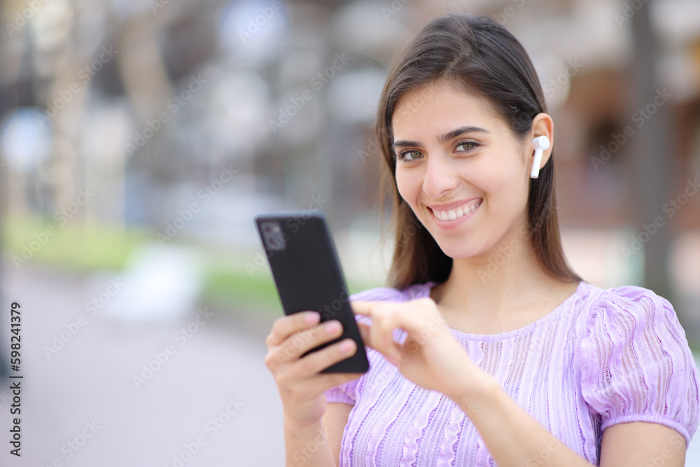 Happy woman posing with earbud and phone Happy woman posing with earbud and phone