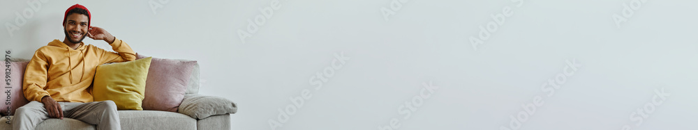 Obraz premium Happy African man looking at camera while sitting on the couch against the wall