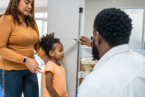 Foto Mature doctor measuring black African little girls height in hospital