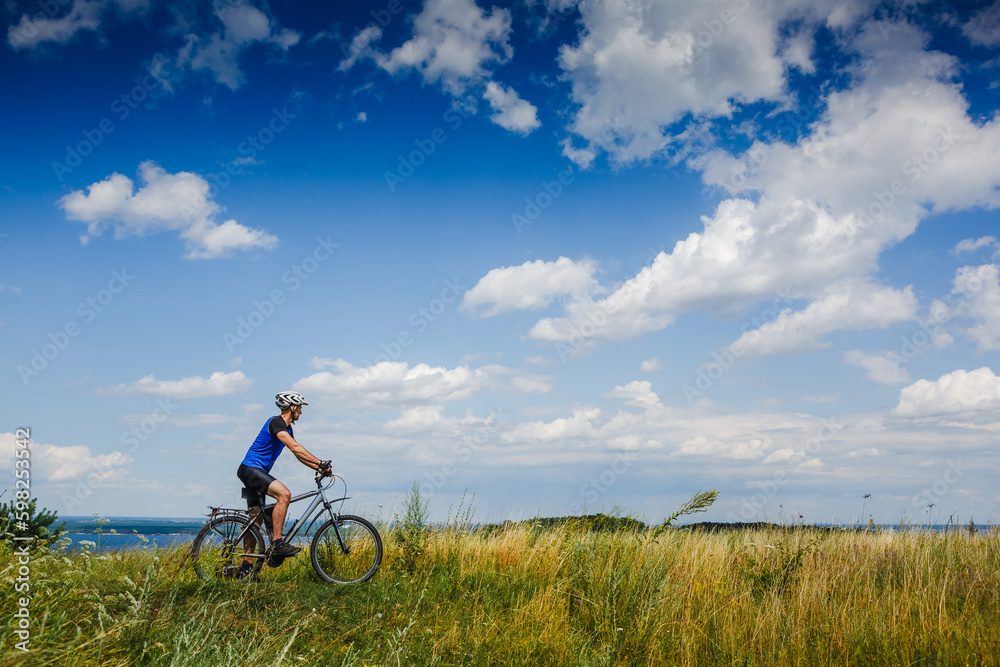 young athletic man on a bicycle riding the green meadow trail on sunny day