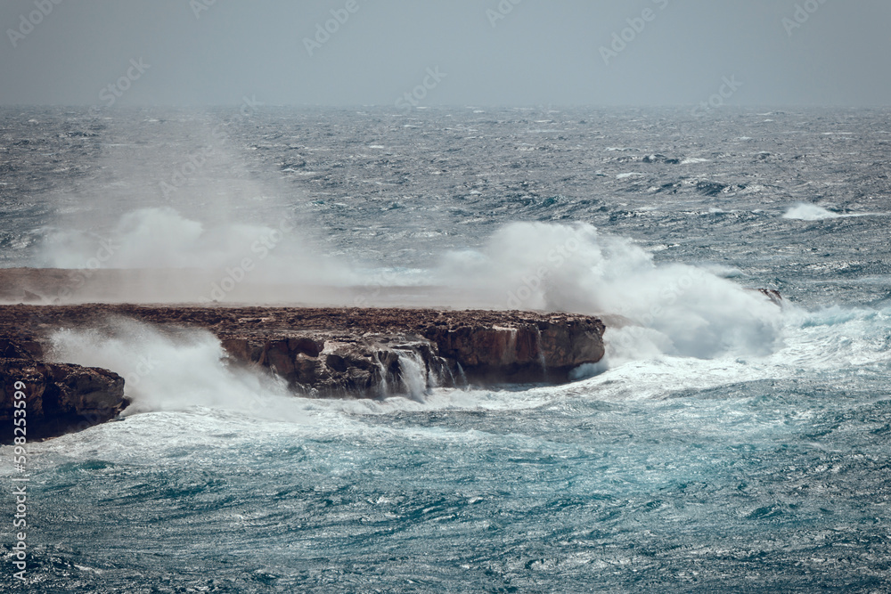 Dramatic seascape. Storm in the ocean, big waves hitting the rocks. Big splashes from the waves hitting the rocks