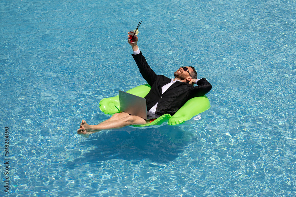 Freelance work, distance online work, e-working. Summer business. Business man in suit drink summer cocktail and using laptop in pool. Business man dreams on summer business in swimming pool water.