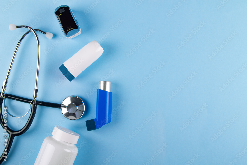 Top view of stethoscope, oximeter, bottle of pills and inhalers on blue ...