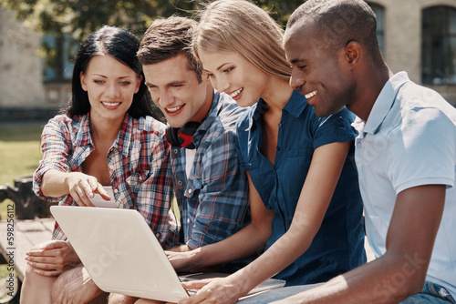 Group of happy students using laptop while spending time outdoors together