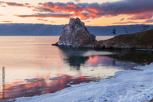 Spring sunset on Baikal Lake. View of the famous Shamanka Rock - a natural landmark of Olkhon Island during the May ice drift. Natural background. Travel and outdoor recreation