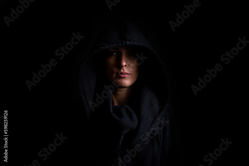 Obraz na plátně Young woman in a black hood on a black background
