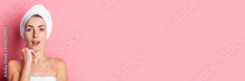 surprised young woman with a towel on her head on a pink background. Banner.