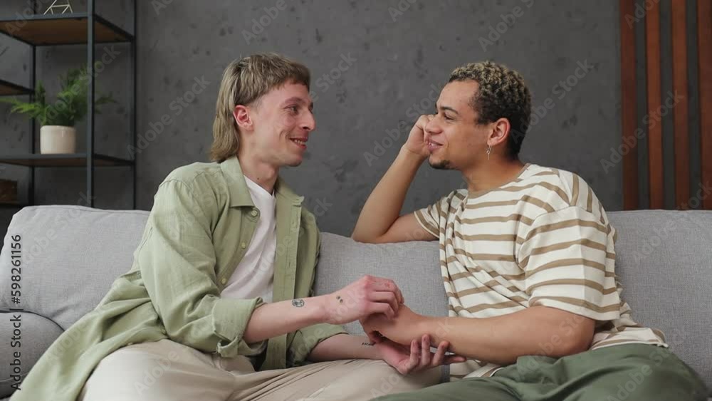 Young happy couple two gay men wear casual clothes sits on sofa talk speak couch stay at home hotel flat rest relax spend free spare time in living room indoor. Pride day june month love lgbtq concept Young happy couple two gay men wear casual clothes sits on sofa talk speak couch stay at home hotel flat rest relax spend free spare time in living room indoor. Pride day june month love lgbtq concept