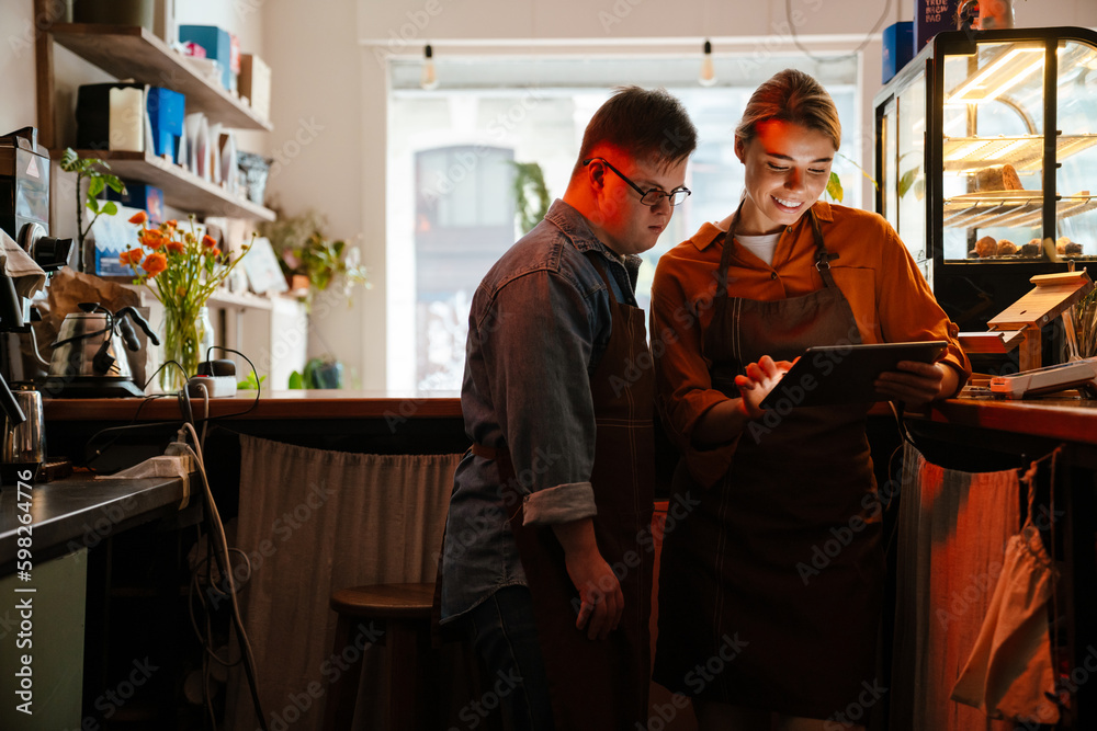 Woman teaching man with down syndrome how to use tablet during internship in cafe Woman teaching man with down syndrome how to use tablet during internship in cafe