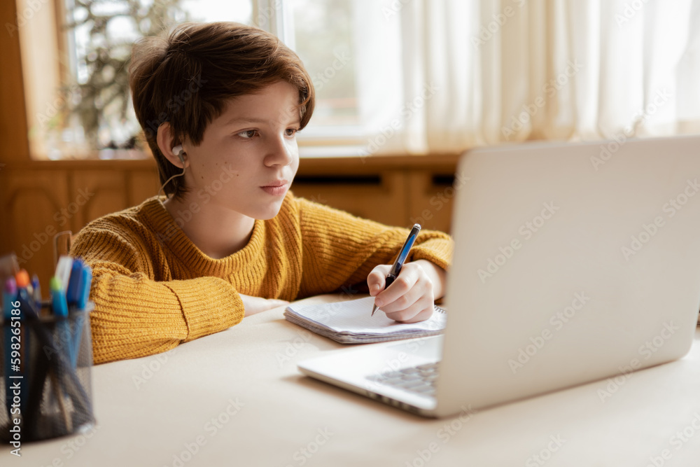 A smiling boy is comfortable learning at home on the computer at an online school A smiling boy is comfortable learning at home on the computer at an online school