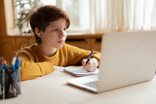 A smiling boy is comfortable learning at home on the computer at an online school