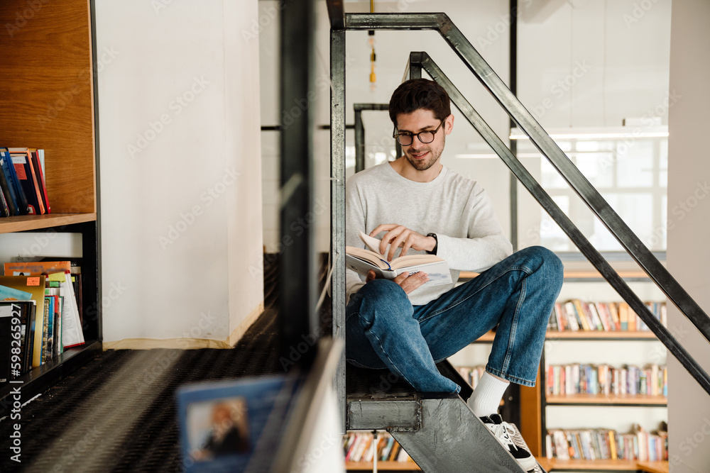 Young man student reading book while sitting in library