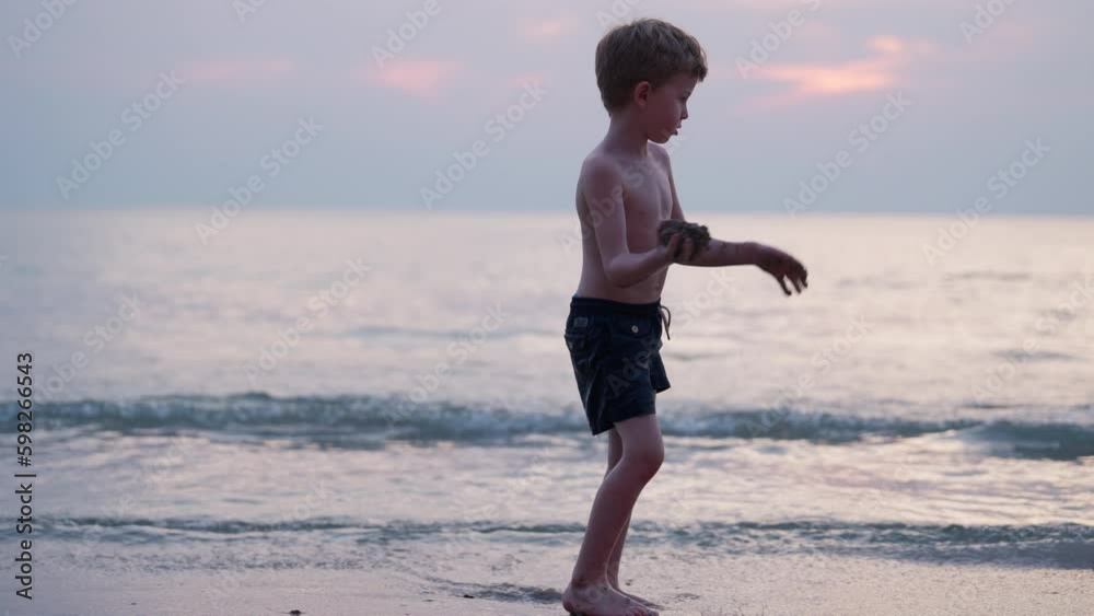 Boy Throwing Sand In Seawater During Sunset