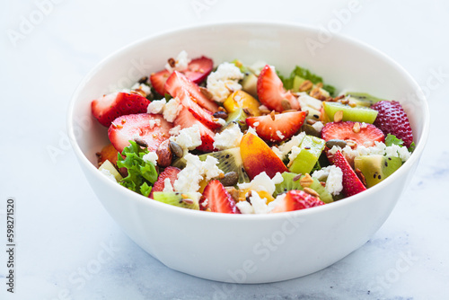 Fruit salad with feta and seeds in white bowl on white table. Healthy vegan detox summer recipe.