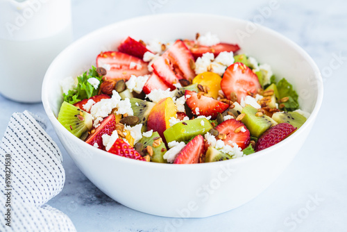 Fruit salad with feta and seeds in white bowl on white table. Healthy vegan detox summer recipe.