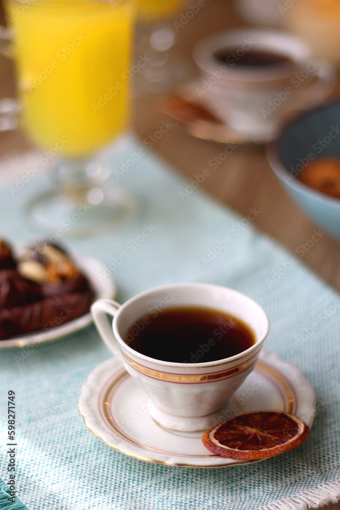 Plate of chocolate pralines, bowl of cookies, cups of tea, glasses of juice and lit candles on the table. Selective focus. Plate of chocolate pralines, bowl of cookies, cups of tea, glasses of juice and lit candles on the table. Selective focus.