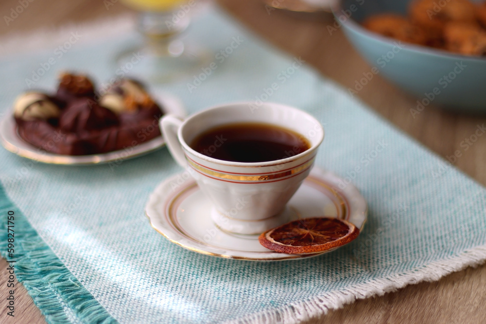 Plate of chocolate pralines, bowl of cookies, cups of tea, glasses of juice and lit candles on the table. Selective focus. Plate of chocolate pralines, bowl of cookies, cups of tea, glasses of juice and lit candles on the table. Selective focus.