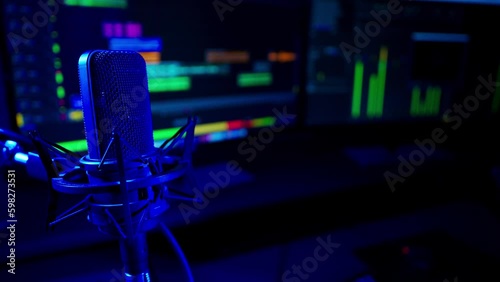 Close shot of a professional studio condenser microphone with audio editing software recording in soft-focus in the background. The sound recording studio is lit with a deep blue light. photo