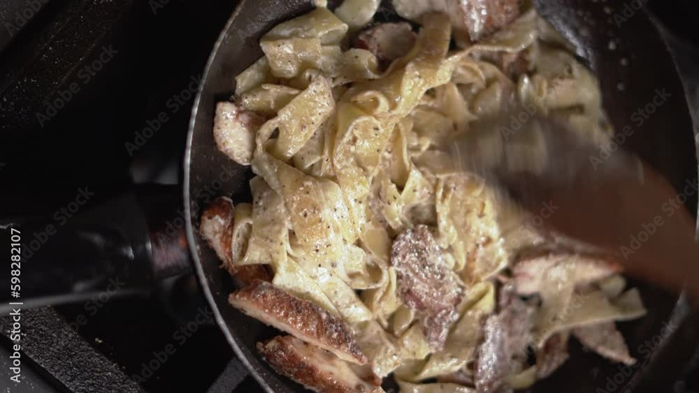 Penne pasta with creamy sauce, chicken and bacon in a skillet. the cook stirs with a wooden spatula. Penne pasta with creamy sauce, chicken and bacon in a skillet. the cook stirs with a wooden spatula.