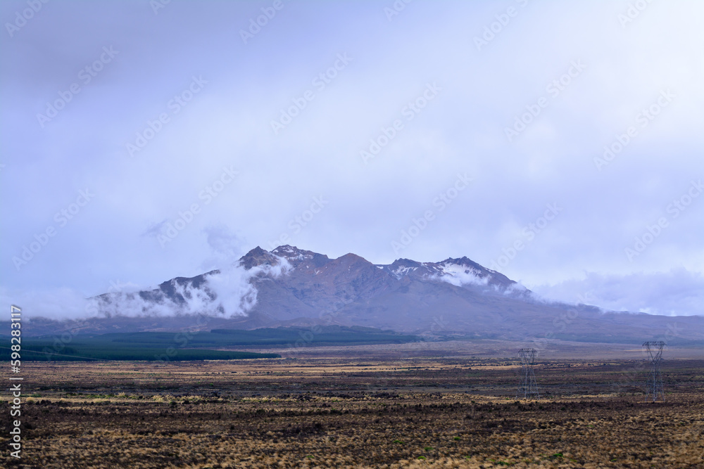 Obraz premium Snow patched peaks of Mt Ruapehu barely visible in the low clouds. Desolated high land field in Central Plateau of New Zealand. Tongariro National Park, North Island