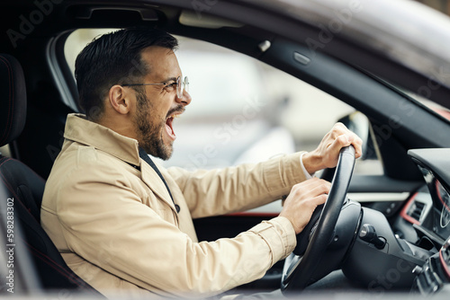 An angry trendy businessman is honking at other drivers in traffic.