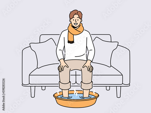 Smiling man in scarf sit on sofa at home soak feet in hot water. Happy male suffer from cold or flu do procedures for fast recovery. Healthcare. Vector illustration.  Generative AI