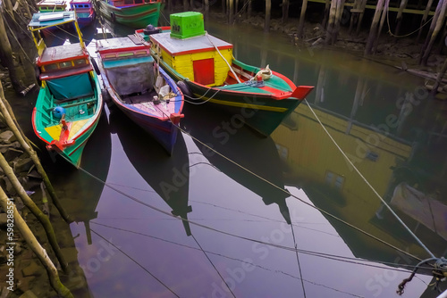 Many small passenger ships is at anchor between wooden buildings in shallow water. Colorful fishing boats in harbor during the day. Small engine boats. photo