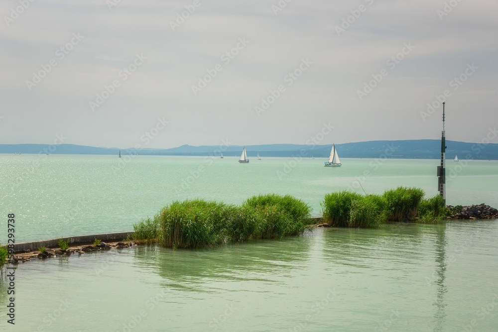 Obraz premium Scenic view of Lake Balaton in Hungary, summer landscape with green water, cozy settlement, yachts and sky, outdoor travel background