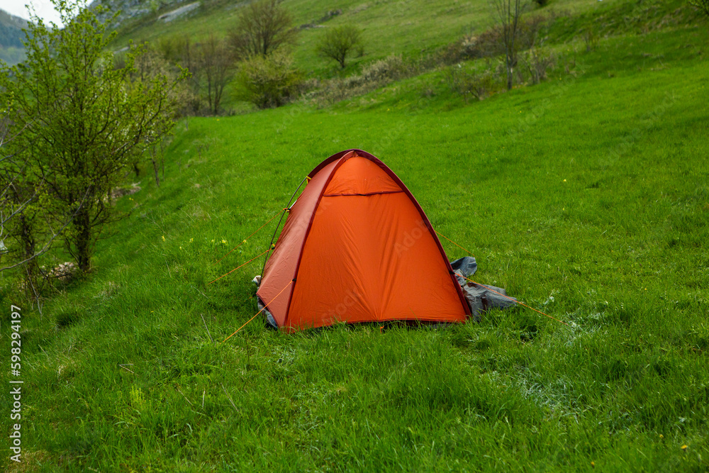 Camping tents on a green meadow in the mountains in spring. Rest with the tent in nature