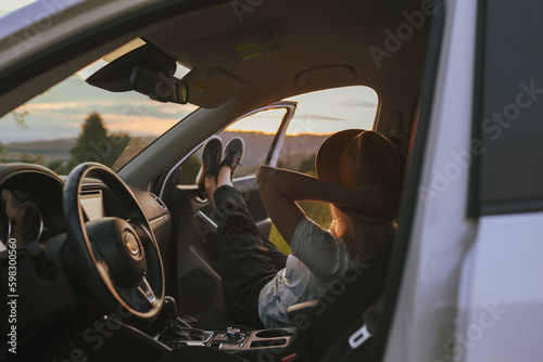 Anonymous young blonde woman in hat sitting in a rental car. Relaxed girl sitting in the car and traveling around in the countryside