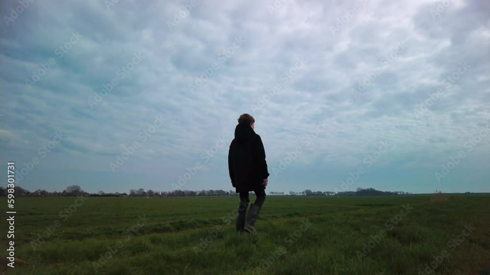 Walking Boy Alone on Grass Trail by Green Meadows and Fields in rural landscape. Outdoor Activities Travel Concept, Hiking Child in Nature on cloudy day, Slow Motion Right Side View Wide shot Walking Boy Alone on Grass Trail by Green Meadows and Fields in rural landscape. Outdoor Activities Travel Concept, Hiking Child in Nature on cloudy day, Slow Motion Right Side View Wide shot