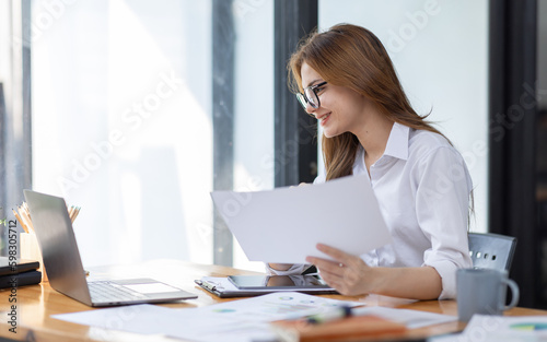 Asian Business woman using calculator and laptop at workplace doing math finance on an office desk, tax, report, accounting, statistics, and analytical research concept