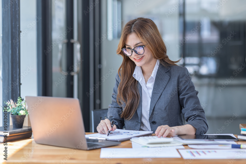 Asian Business woman using calculator and laptop at workplace doing math finance on an office desk, tax, report, accounting, statistics, and analytical research concept