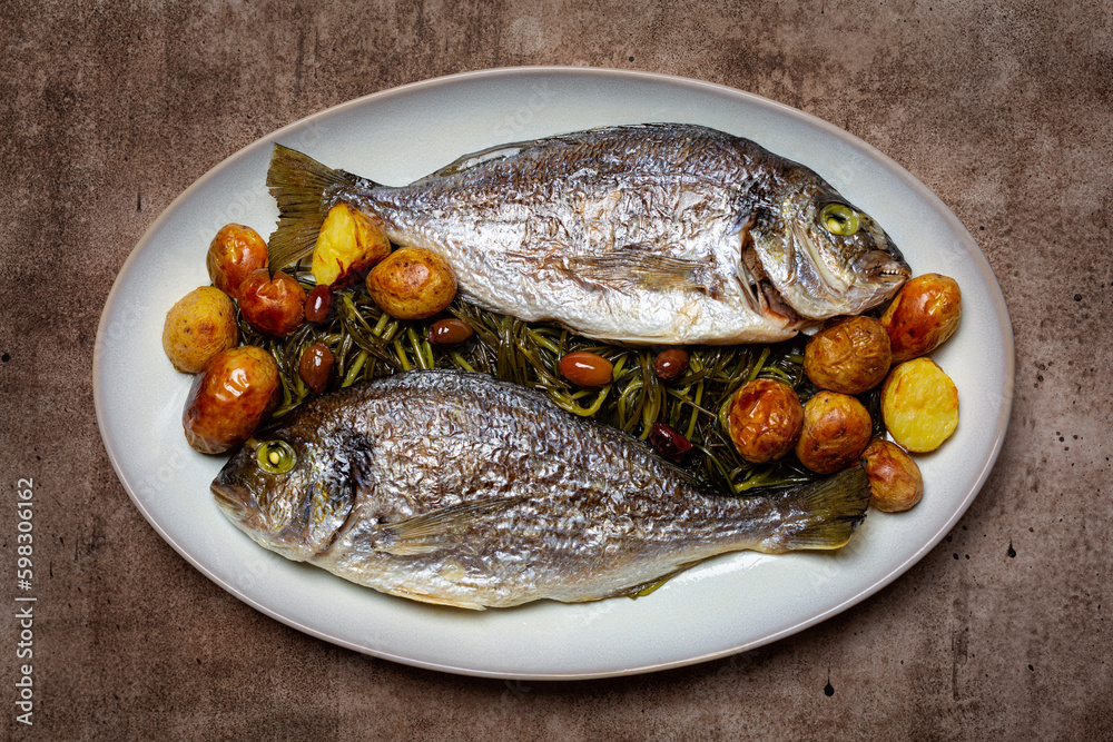 Baked whole gilt head sea bream, also known as dorada or orata fish, with agretti, olives and spring potatoes ,  Mediterranean food, healthy dish.