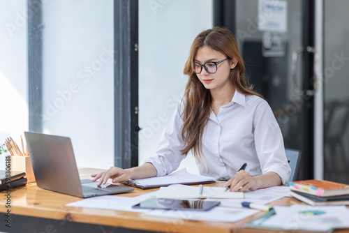 Asian Business woman using calculator and laptop at workplace doing math finance on an office desk, tax, report, accounting, statistics, and analytical research concept