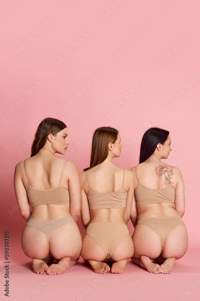 Naklejka premium Portrait with group of young girls, women wearing beige inner wear sitting on pink studio background. Beauty of female body