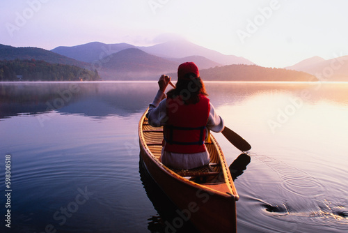 United States, New York, Rear view of woman paddling canoe on Lake Placid at sunrise, Adirondacks State Park photo