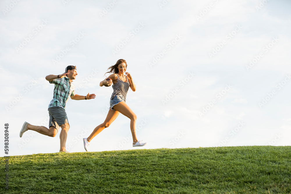 Woman and man running on grassy hill in park Woman and man running on grassy hill in park