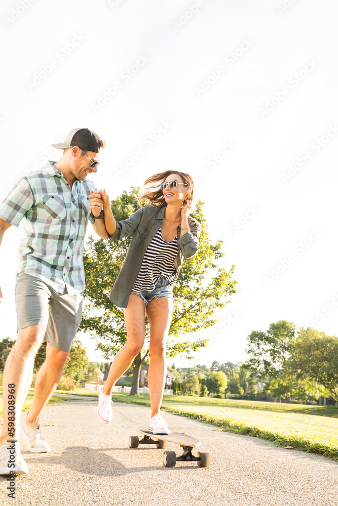 Man helping woman to balance while riding longboard Man helping woman to balance while riding longboard