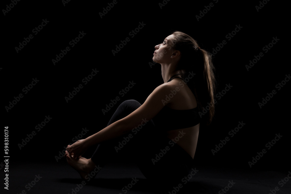 Obraz premium cute caucasian girl relaxing after yoga exercise against dark backgroung. side lit silhouette.