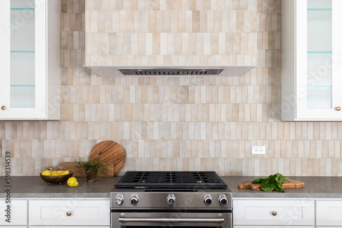 Foto A kitchen oven and hood detail with brown rectangle tiles, stainless steel oven, white cabinets, and cozy decor on grey stone countertops