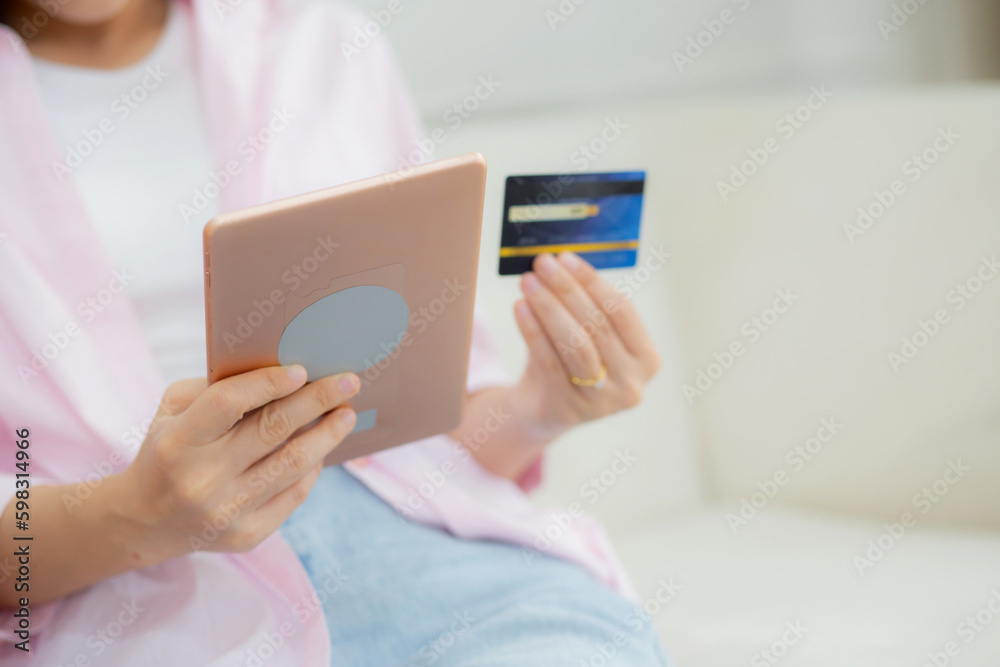 Hands of young asian woman sitting on sofa using digital tablet shopping online with credit card on couch, female paying with transaction financial, purchase and payment, business concept.