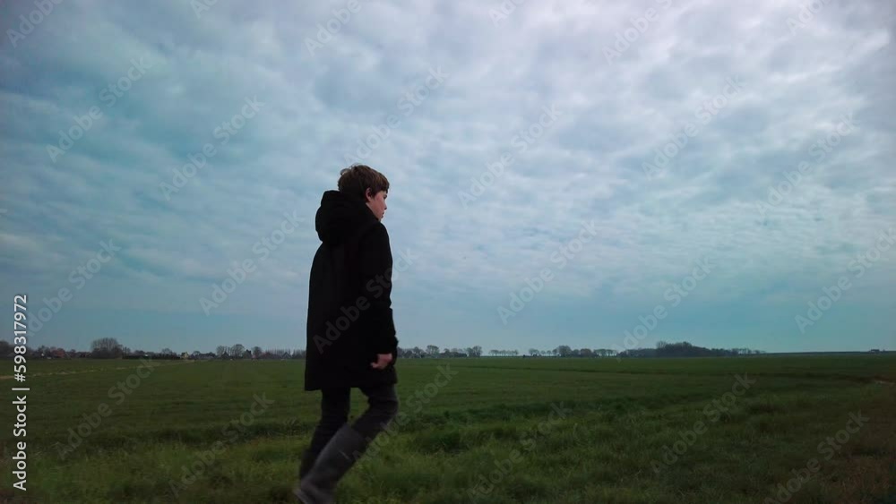 Serious thoughtful look walking boy, hiker in nature rural scenery, dramatic cloudscape. Lonely child looking into the distance. People and environment concept Low angle right side view slow motion Serious thoughtful look walking boy, hiker in nature rural scenery, dramatic cloudscape. Lonely child looking into the distance. People and environment concept Low angle right side view slow motion